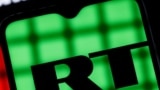Behind bars is a smartphone with the RT (Russia Today) logo on the background of the Youtube logo. Blocking RT (Russia Today) YouTube channels.